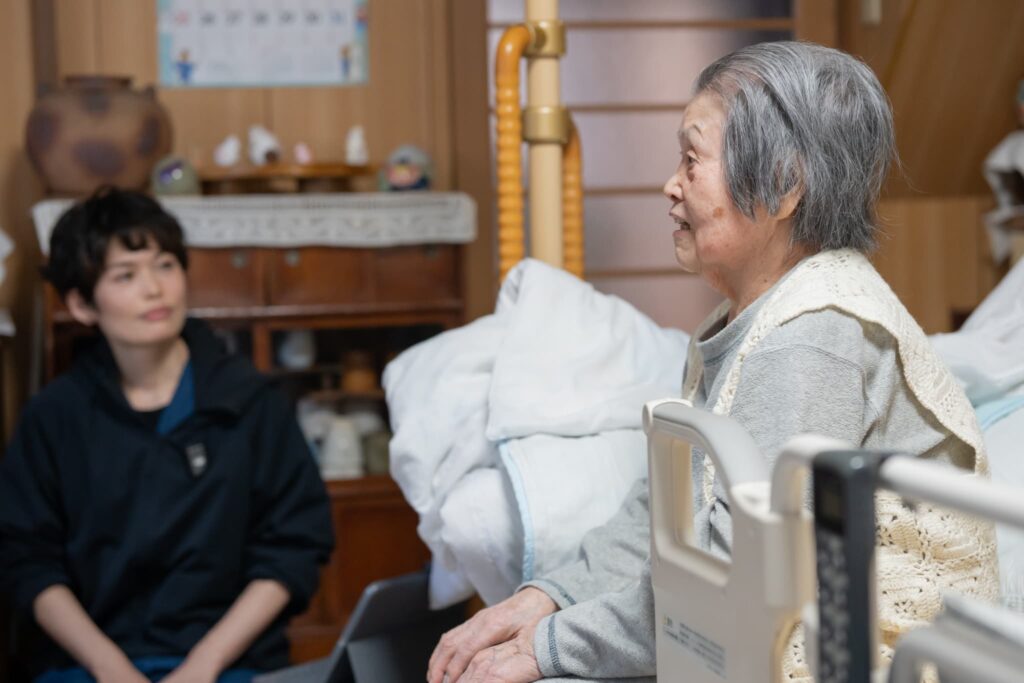 ベッドに座って話す高齢女性と話を聞く女性医師
